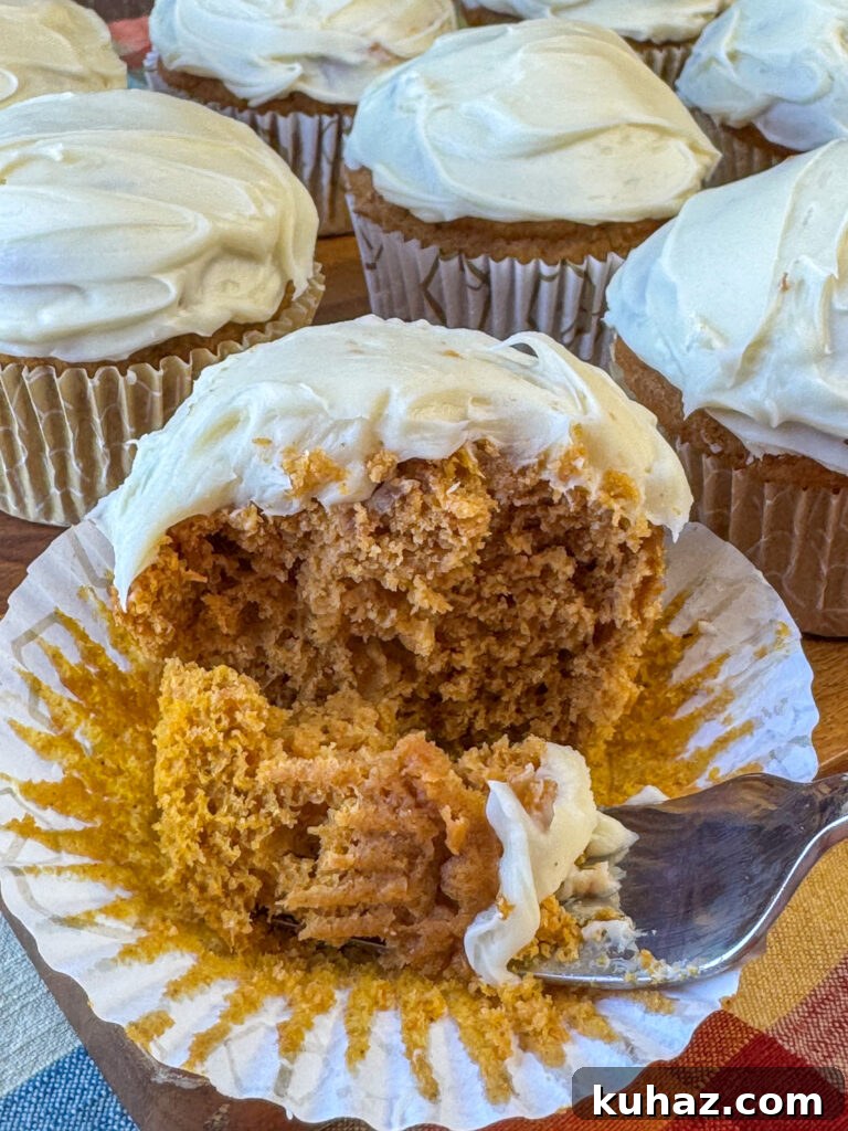 Pumpkin Spice Cupcake Recipe with Cream Cheese Frosting 3 Cream cheese frosting coating pumpkin spice dessert with a fork that took a bite on a red, yellow and orange plaid napkin.