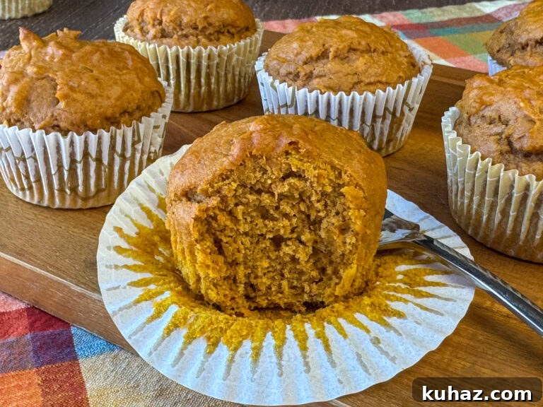 Pumpkin Spice Cupcake Recipe with Cream Cheese Frosting 8 Pumpkin spice cupcake with the liner pulled down around the edges and a fork taking a bite out showing how moist and flavorful the box mix pumpkin spice dessert is with more cupcakes in the background.