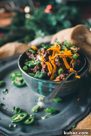 How to Grill Tender Elk Steaks with Smoky Flavor 11 A bowl of venison chili topped with sliced green onions and shredded cheese, garnished with jalapeño slices.