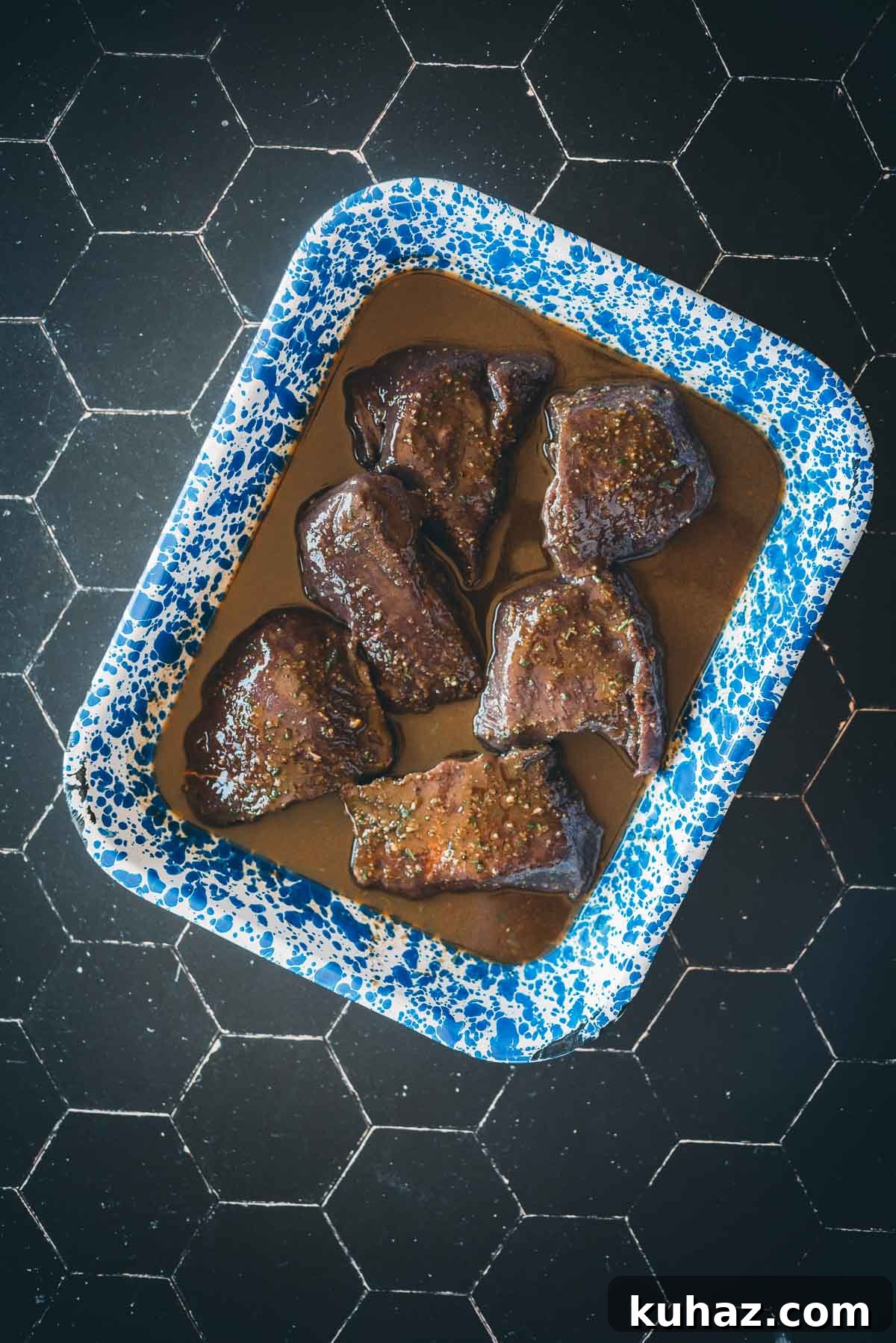 How to Grill Tender Elk Steaks with Smoky Flavor 5 A blue-speckled tray contains six pieces of marinated elk in a balsamic marinade.