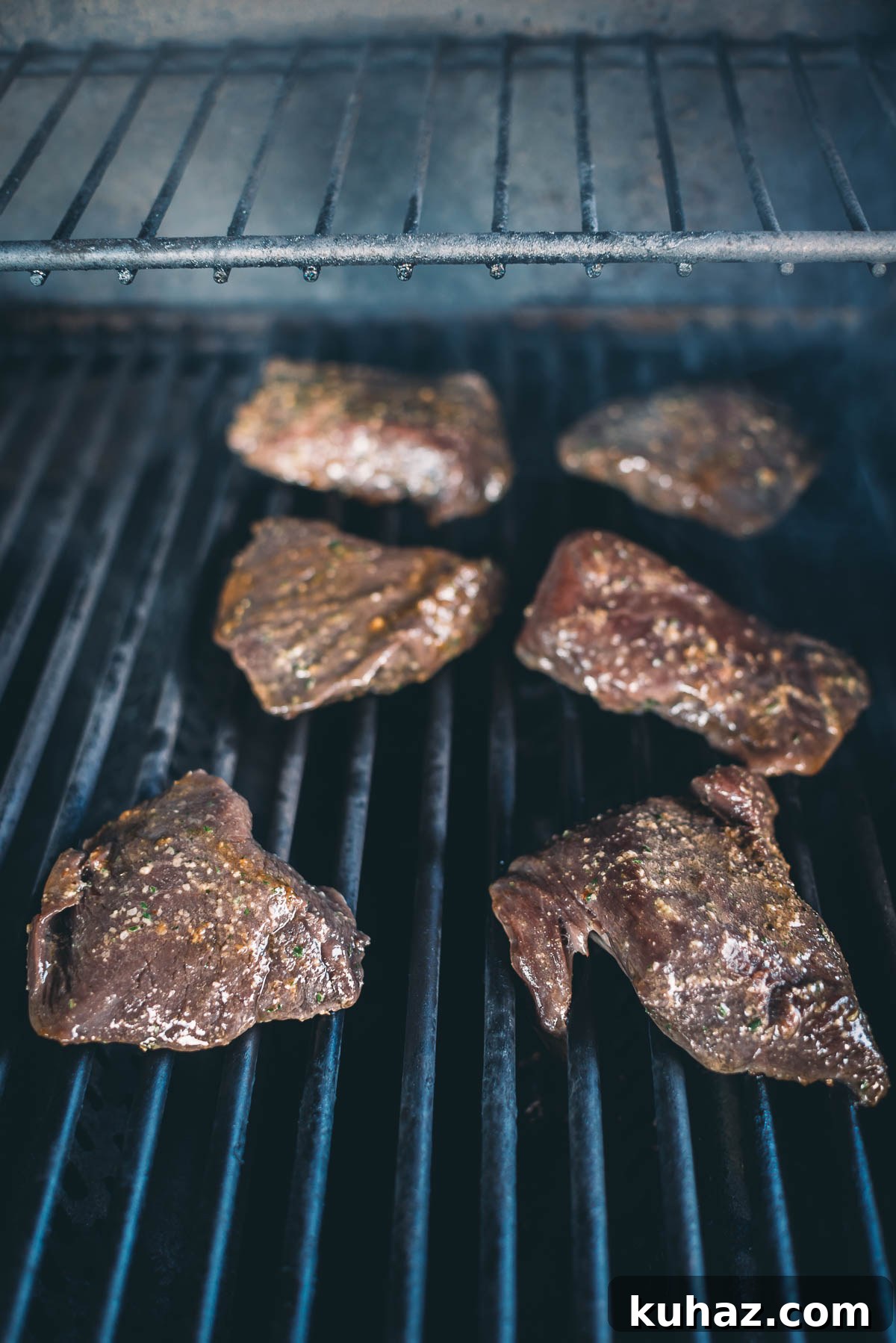 How to Grill Tender Elk Steaks with Smoky Flavor 6 Six pieces of marinated elk steaks being grilled on a barbecue with visible grill marks.