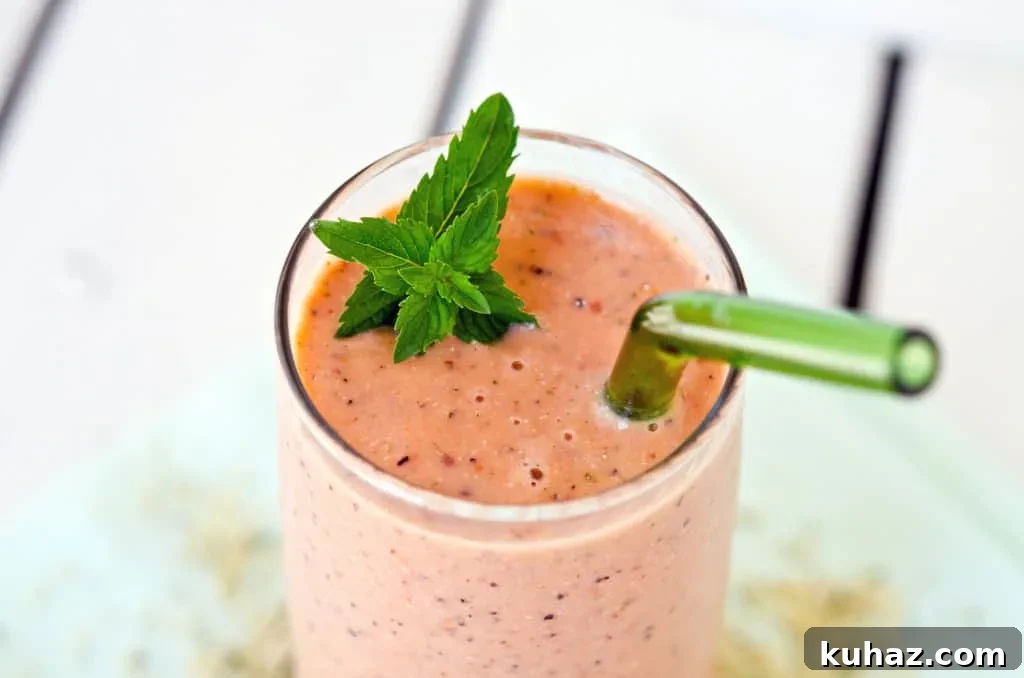 Mint Melon Peach Smoothie close up of pink-hued smoothie in a glass, garnished with mint, and a green straw