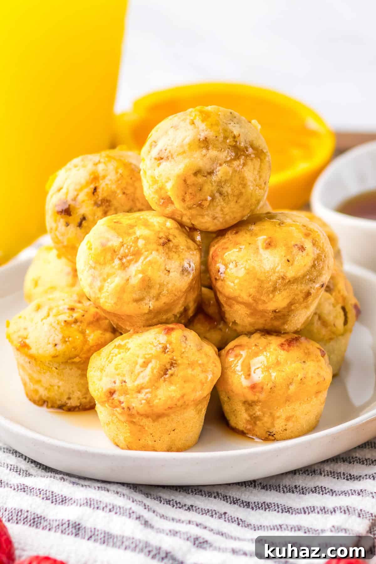 Savory Breakfast Sausage Pancake Muffins 2 Mini sausage pancake muffins stacked on a plate, glistening with syrup. A glass of orange juice and syrup dish are blurred in the background.