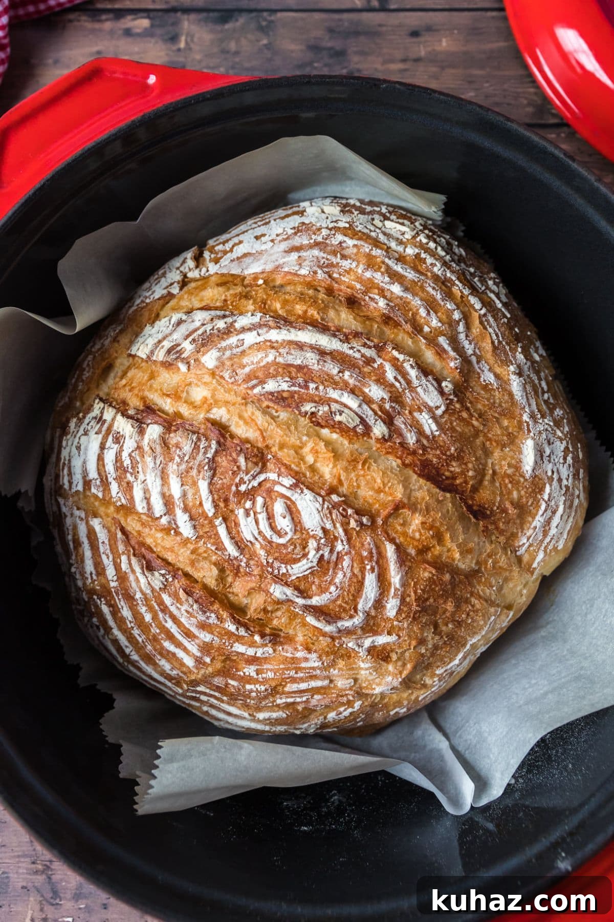 Round golden brown artisan sourdough bread baked in a red dutch oven