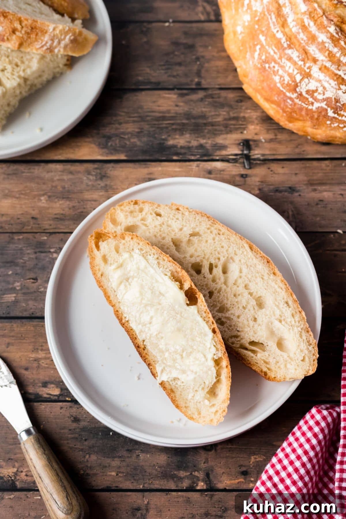 Sourdough slices of bread with butter on a white plate, placed on a wooden table