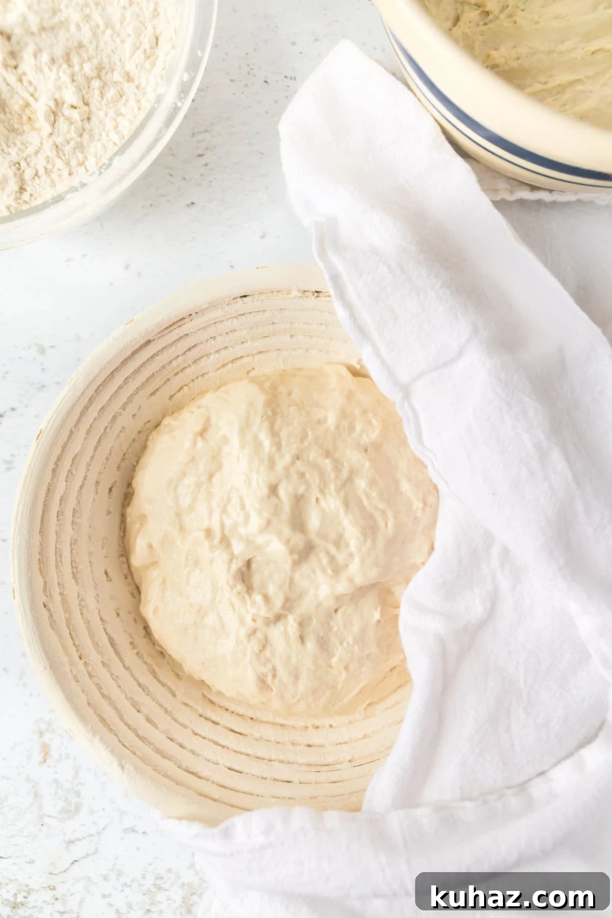 Sourdough bread getting ready to rise in a banneton proofing basket covered with a white linen.