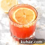 A guava mocktail garnished with a lemon slice and coconut rim.