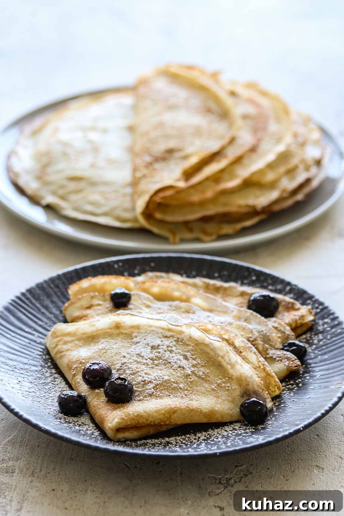 How to Make Sourdough Discard Crepes 2 Two plates of sourdough crepes, one plain, one with icing sugar and blueberries.