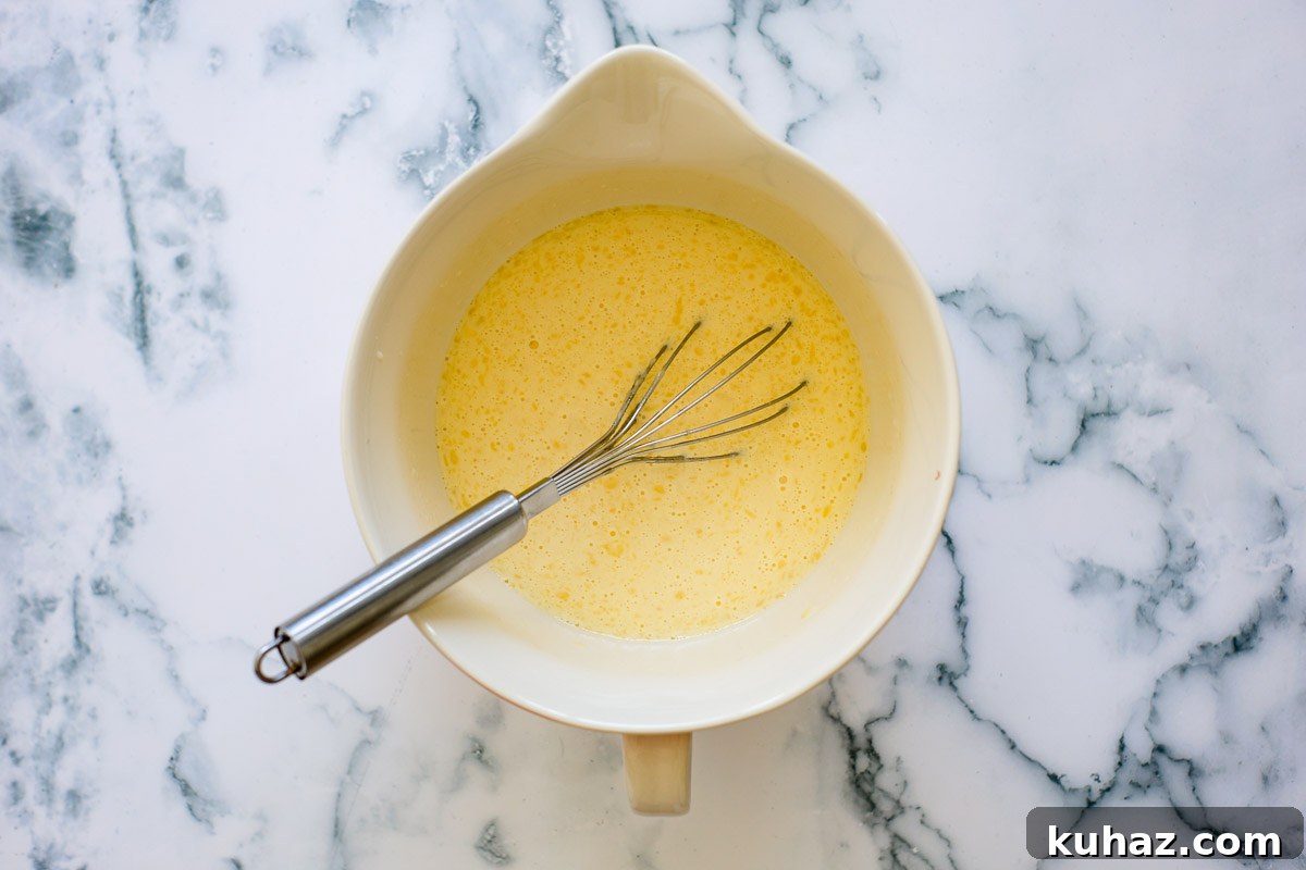 How to Make Sourdough Discard Crepes 5 Wet ingredient with whisk inside a ceramic bowl.