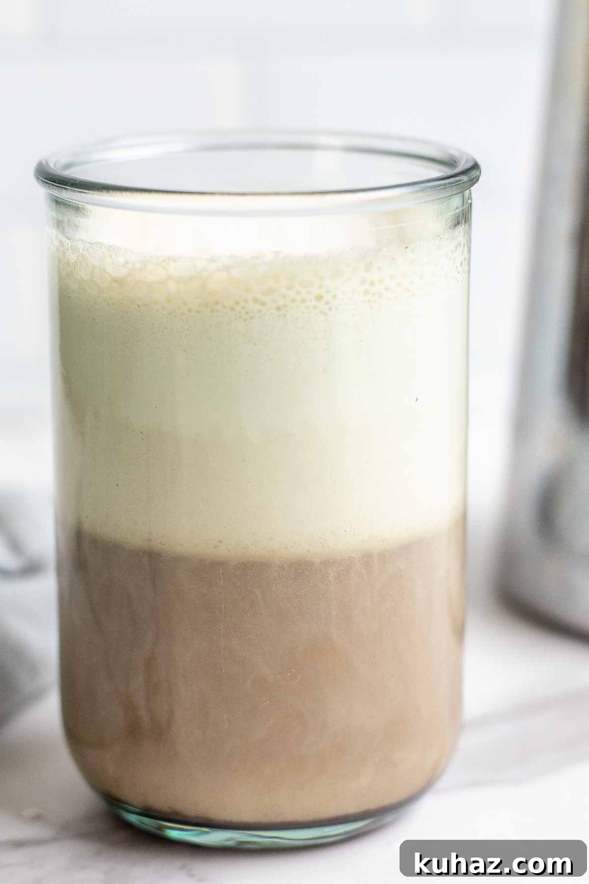 How to Make Sweet Cream Cold Foam at Home 2 close up photo of coffee topped with cold foam in a glass with a French press in the background.