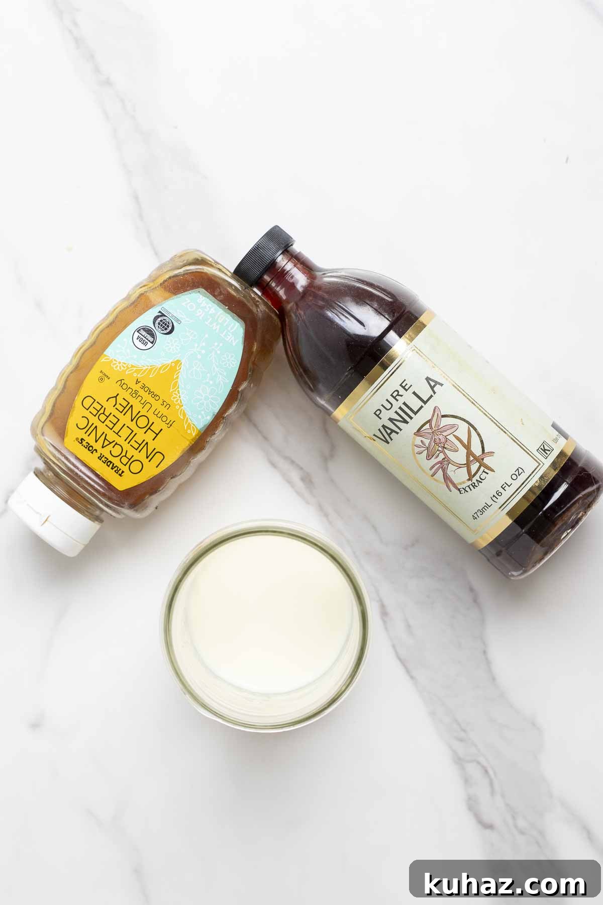 How to Make Sweet Cream Cold Foam at Home 4 a bottle of honey, a bottle of vanilla extra, and a jar of milk on a marble counter.
