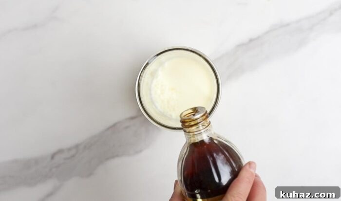How to Make Sweet Cream Cold Foam at Home 5 vanilla extract being added to a jar with milk on a marble countertop.