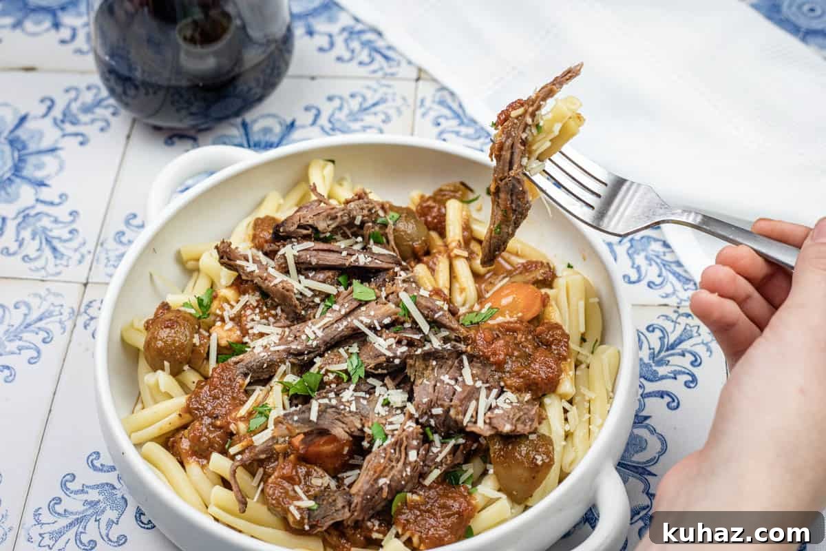 17 Authentic Italian Dinner Recipes Even Nonna Will Love 3 A hand lifting a fork with a bite of Italian Pot Roast Pasta on a bowl.