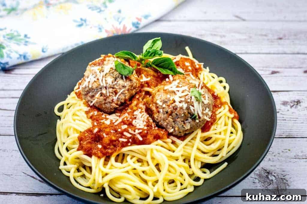 17 Authentic Italian Dinner Recipes Even Nonna Will Love 5 A plate of spaghetti topped with two meatballs, marinara sauce, grated cheese, and basil garnish.