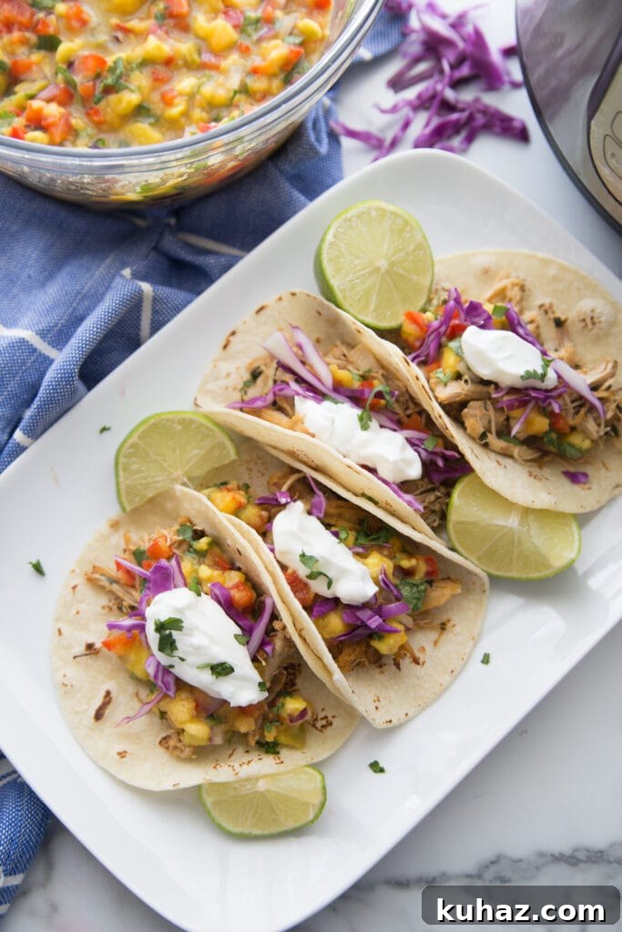 Instant Pot Chicken Carnitas with Avocado Peach Salsa Recipe 2 A white plate of tacos made from instant pot chicken carnitas with avocado peach salsa sitting nearby