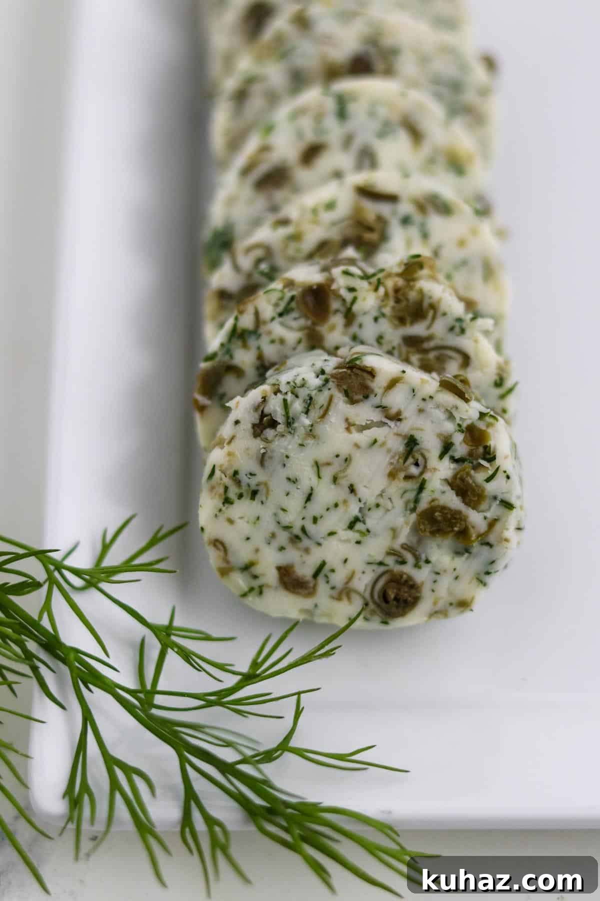 Three-Ingredient Dill and Caper Butter Recipe 2 Rounds of Dill Caper Butter on a square plate next to a dill sprig.