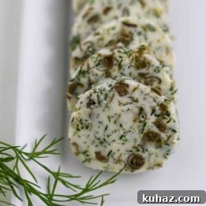 Close up of round of dill caper butter on a plate next to a sprig of dill.