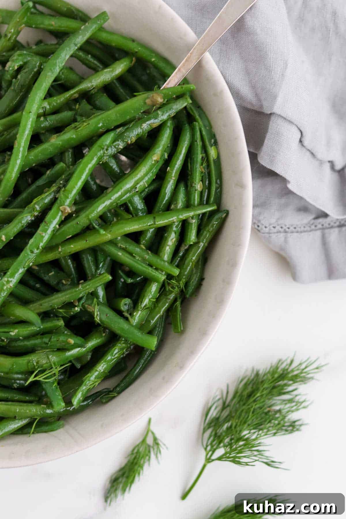 Three-Ingredient Dill and Caper Butter Recipe 7 Green beans in a bowl with a spoon next to dill sprigs and a napkin.