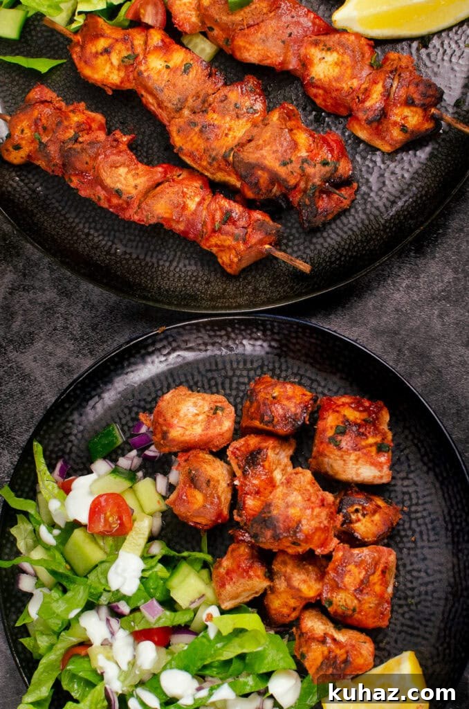 How to Make Authentic Tandoori Chicken Tikka Kebabs 2 Tandoori Chicken Tikka Kebab skewers on a black plate and cubes of tikka chicken served with a side salad on another black plate