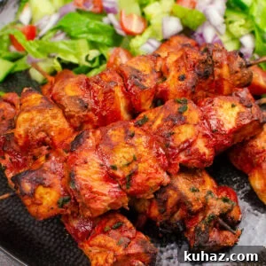 How to Make Authentic Tandoori Chicken Tikka Kebabs 3 Tandoori Chicken Tikka Kebab skewers served on a black plate with salad on the side