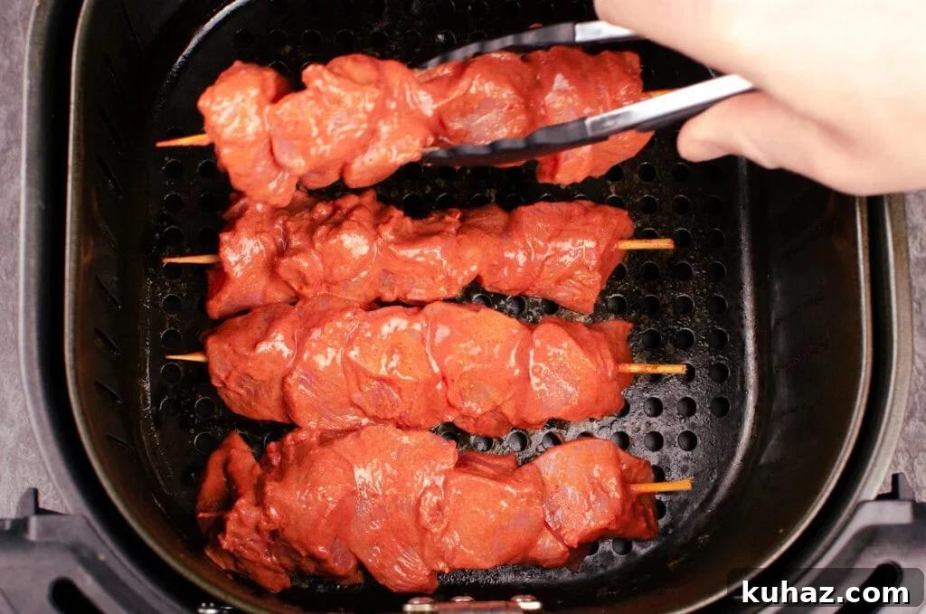 How to Make Authentic Tandoori Chicken Tikka Kebabs 10 Placing chicken tikka kebabs into an air fryer with black and silver tongs