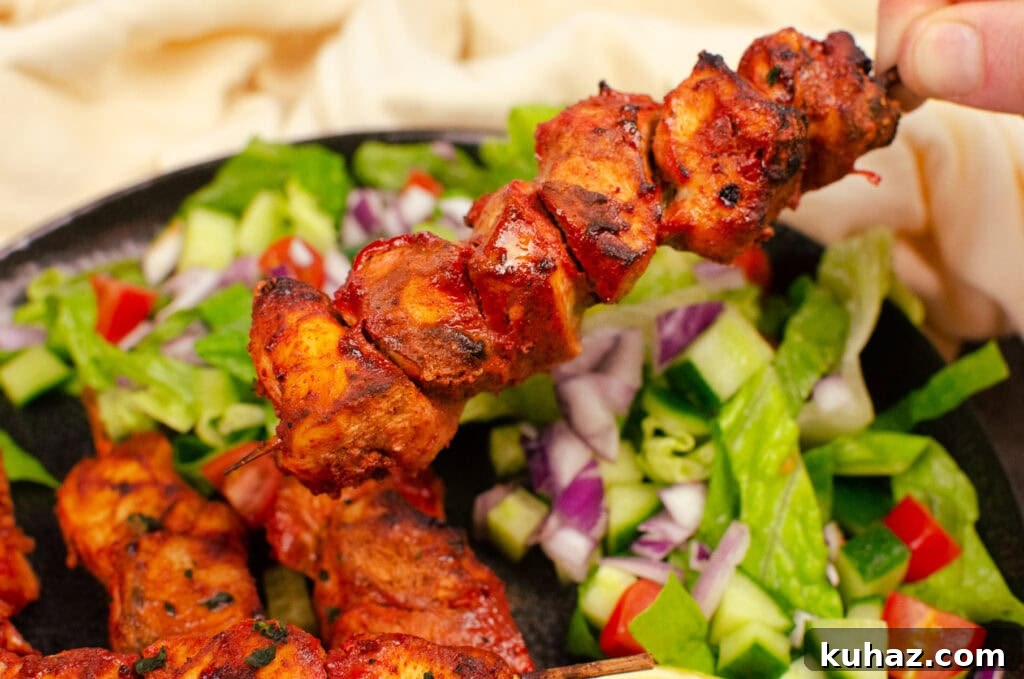 How to Make Authentic Tandoori Chicken Tikka Kebabs 14 Dry chicken tikka kebabs being picked up by hand with a side salad in the background